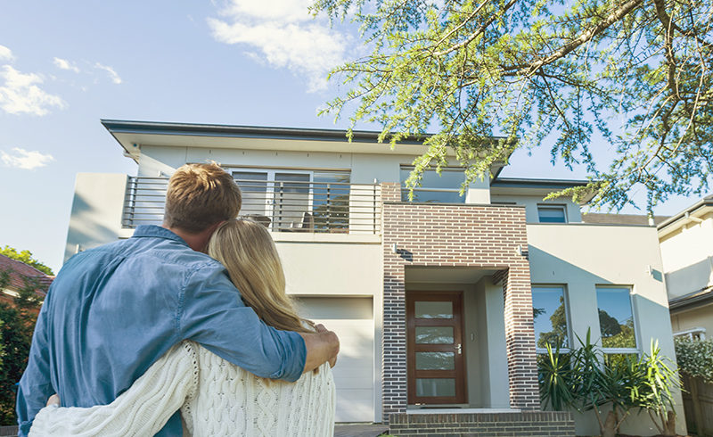 couple standing in front of new home with large tree in yard